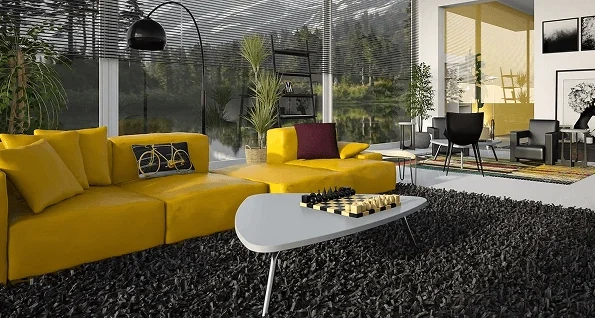 A stylish modern living room featuring a large yellow sectional sofa on a dark shag rug. A white coffee table holds a chess set, and large windows in the background overlook a calm lake.